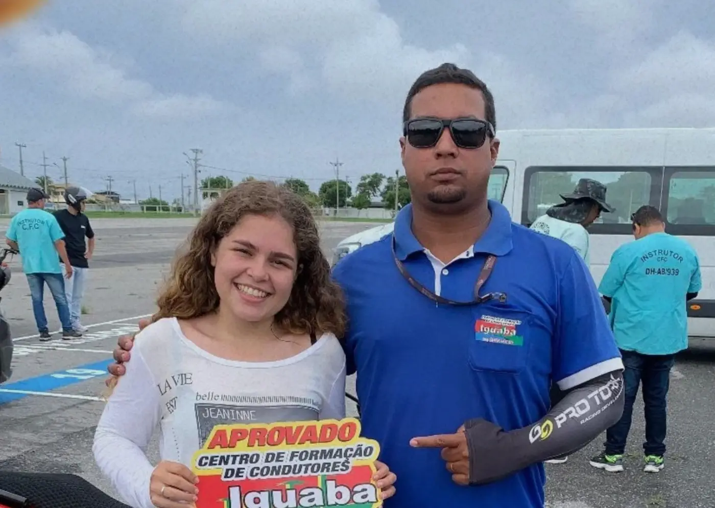 Aluna aprovada segurando a placa da Auto Escola Iguaba ao lado do instrutor